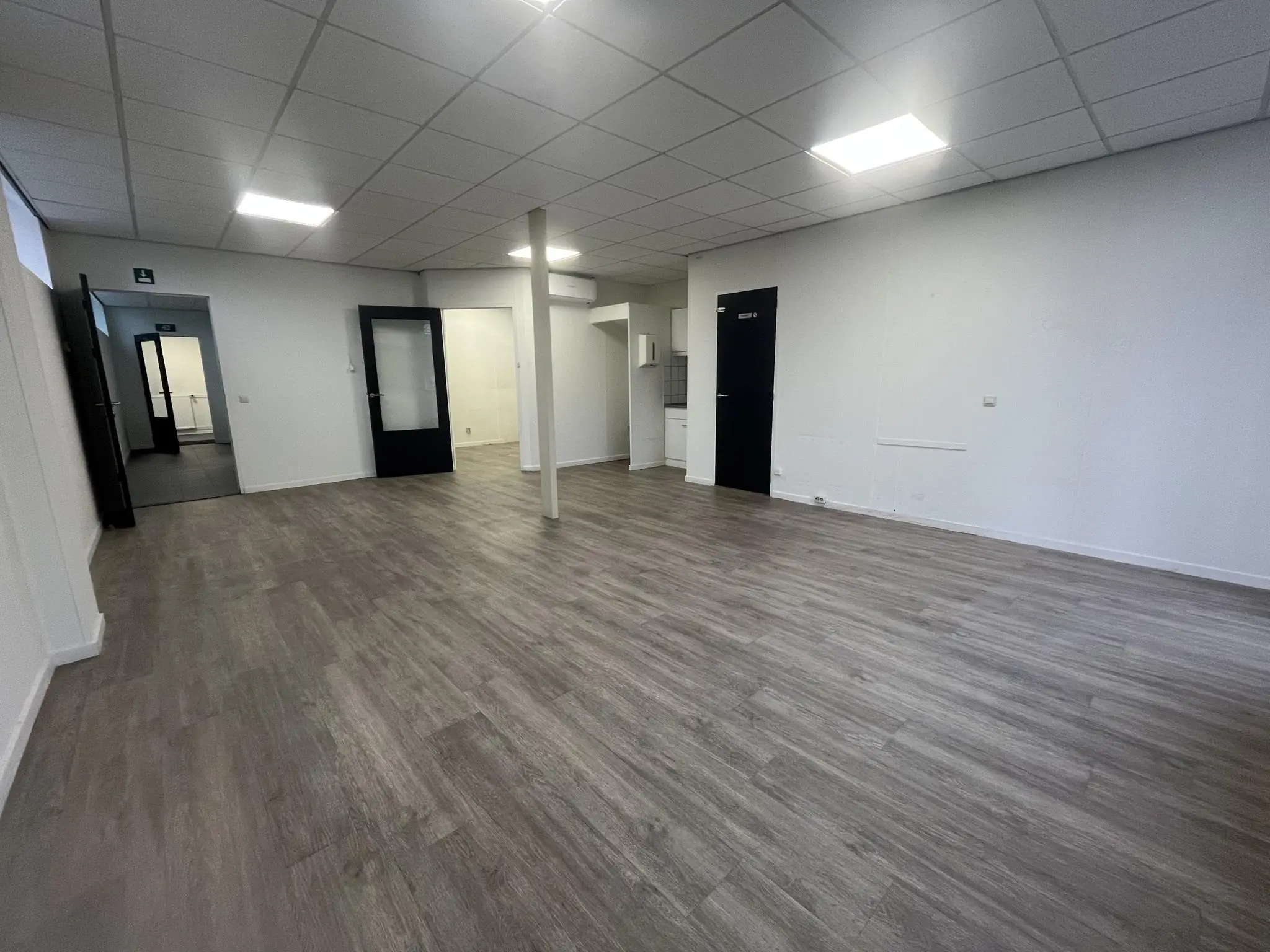 Leegstaand kantoor met grijze vloer, systeemplafond en meerdere zwarte deuren aan de Burgemeester Smitsstraat.